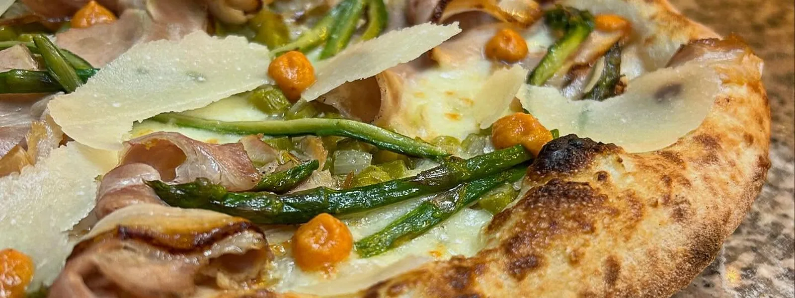 Primo piano del cornicione di una pizza con scaglie di grana e verdure.