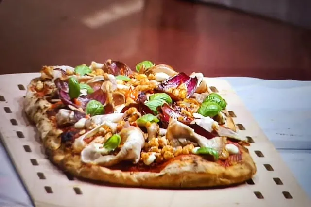Una pizza sulla pala di legno davanti alla bocca del forno.