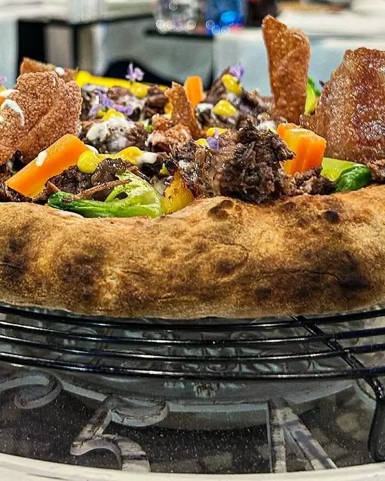 Pizza guarnita con verdure e sfoglie croccanti, su una griglia di raffreddamento.