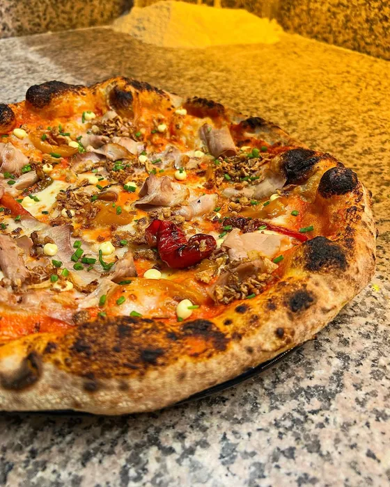 Pizza con salumi, pomodorini ed erbe fresche appoggiata sul banco in marmo.