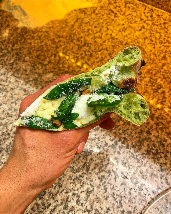 Un trancio di pizza bianca con foglie verdi, tenuto in mano.