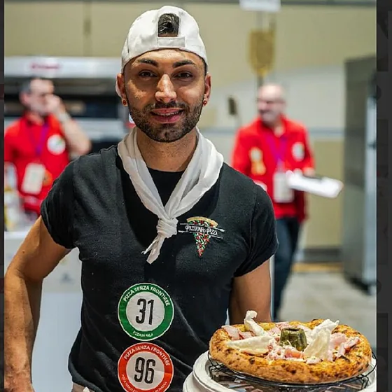 Il pizzaiolo di Passione Pizza con una pizza appena preparata, davanti al forno.